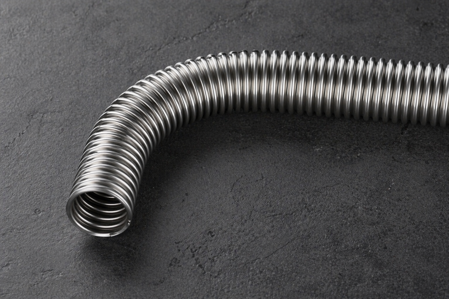 Editorial shot of Ridgeline corrugated stainless steel tube curving across dark stone surface