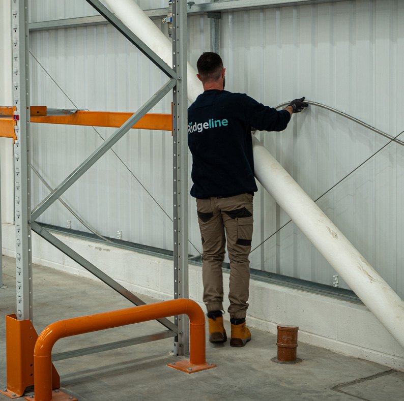 A Ridgeline installer routing corrugated stainless tube along the warehouse structure at Vulcan
