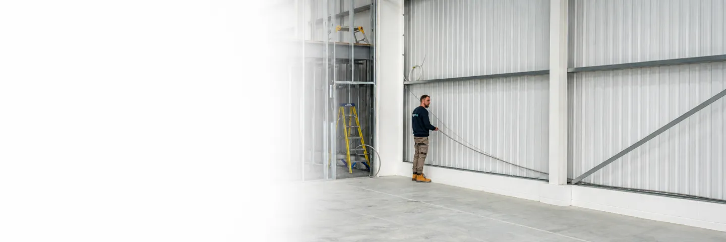 Ridgeline installer routing corrugated stainless steel tube along a commercial steel-clad warehouse wall