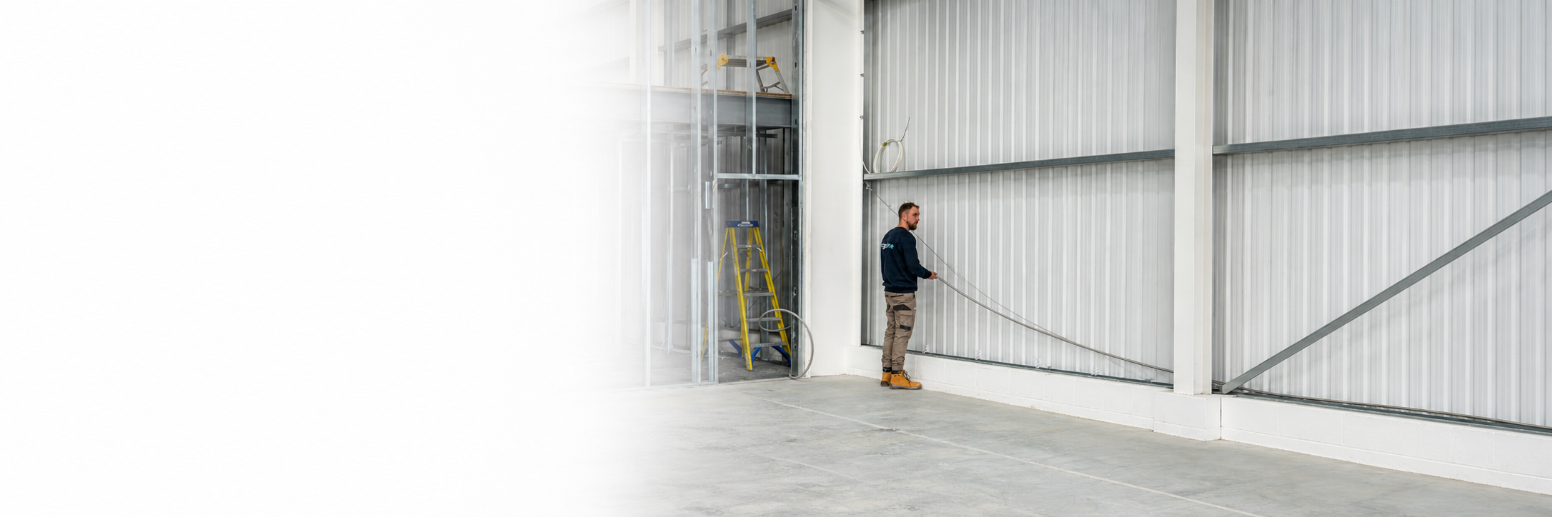 Ridgeline installer routing corrugated stainless steel tube along a commercial steel-clad warehouse wall