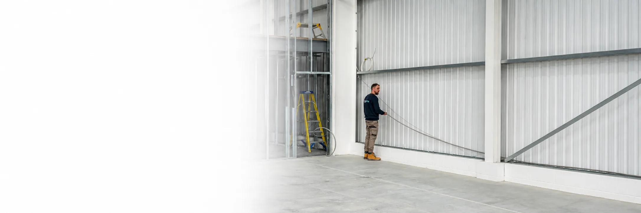 Ridgeline installer routing corrugated stainless steel tube along a commercial steel-clad warehouse wall